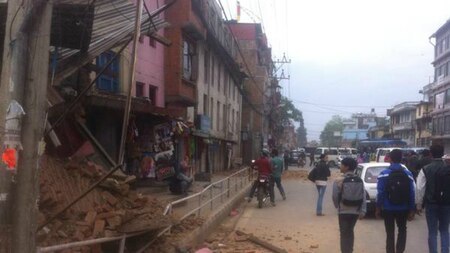 Students walk past an earthquake-ravaged building in a street in Nepal.