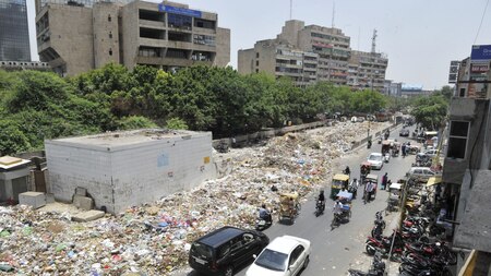 Vehicles ply on what remains of a wide road where garbage continues to pile up