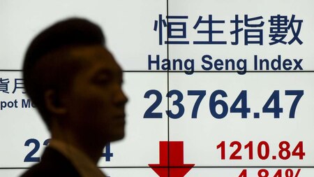 A man walks past a panel displaying the Hang Seng Index