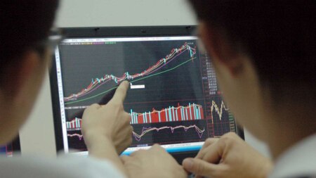 Students point at a laptop screen showing stock information