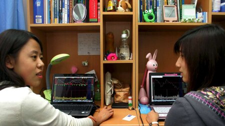 Students sit in front of laptop screens showing stock information