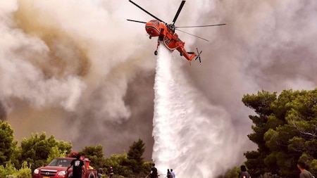 A firefighting helicopter drops water to extinguish flames during a wildfire at the village of Kineta