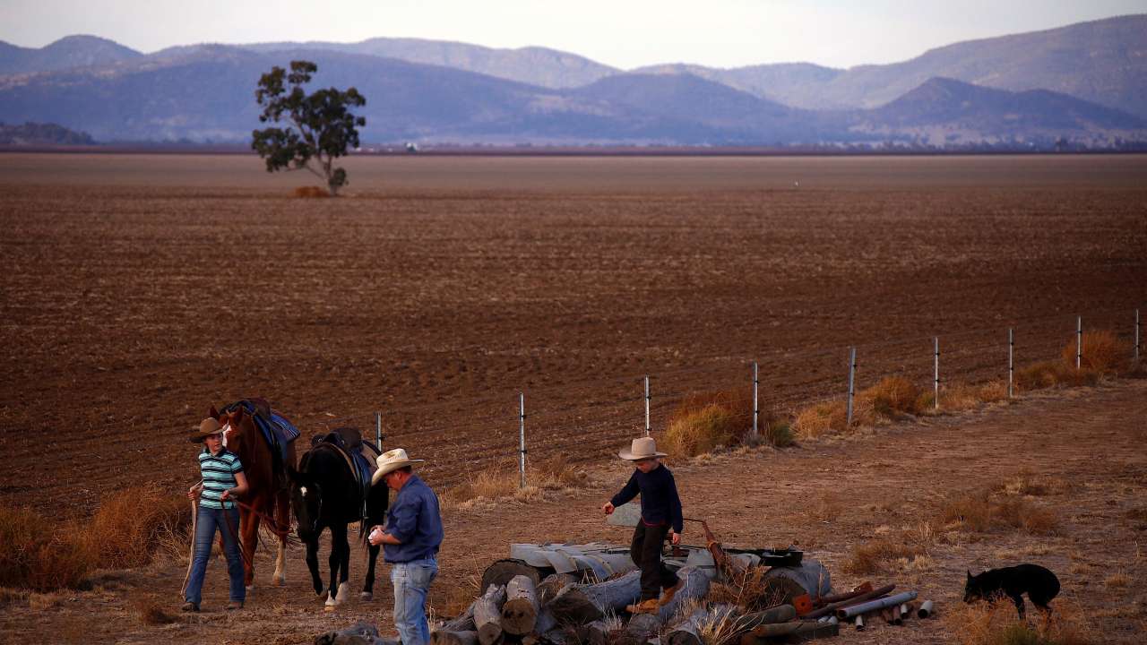 Farmer with his daughter and son walk their horses next to a fence