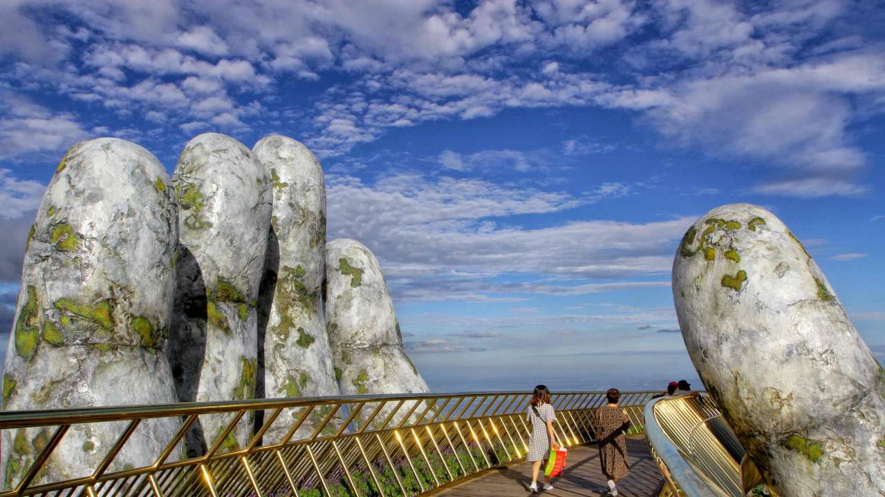 Two giant concrete hands emerge from trees, holding up glimmering golden bridge