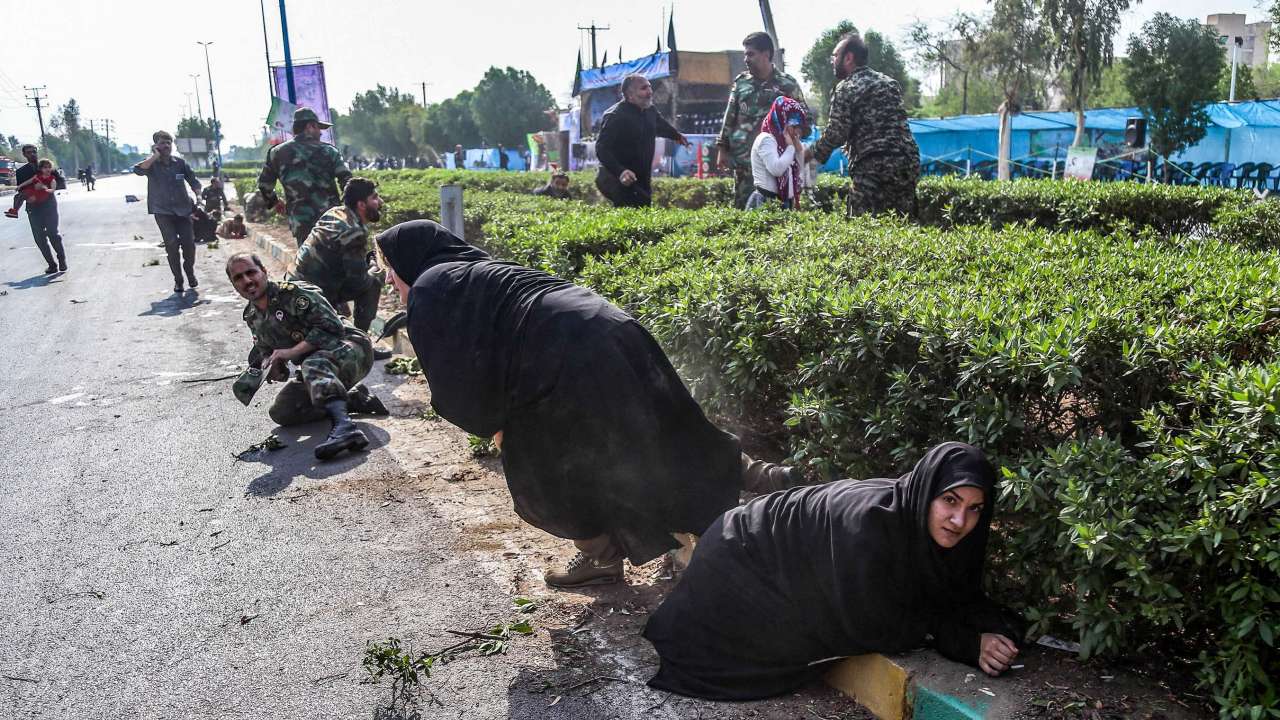 Iranian women and soldiers taking cover next to bushes