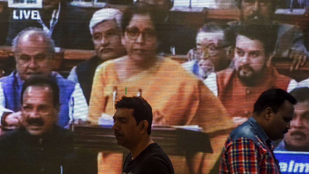 People walk past a screen displaying a television channel live broadcast of Nirmala Sitharaman presenting the 2020 union budget