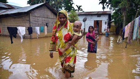 Women wade through waterlogged road at a flood-affected area, in Nagaon district on Wednesday
