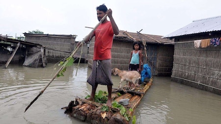A man uses a makeshift raft to cross the flood water at Puthimari village in Darrang